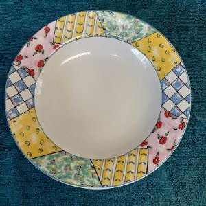 May include: A white ceramic bowl with a colorful patchwork design. The bowl has a yellow, blue, green, red, and pink pattern.