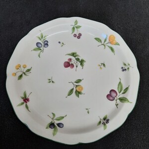 May include: A white ceramic serving platter with a green rim. The platter is decorated with a pattern of various fruits and berries, including strawberries, cherries, plums, and olives.