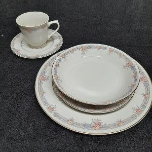 May include: A set of white porcelain dinnerware with a floral pattern. The set includes a large dinner plate, a smaller salad plate, and a teacup with a matching saucer.