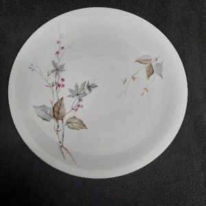 May include: A white ceramic bowl with a floral design featuring pink flowers and brown leaves. The bowl is perfect for serving salads, soups, or desserts.