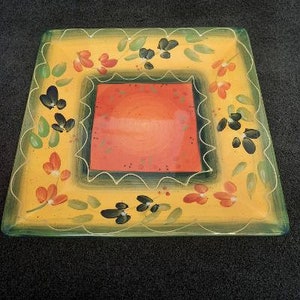 May include: A square ceramic serving platter with a yellow background and a green border. The center of the platter has a red square with a white scalloped border. The platter is decorated with hand-painted flowers and leaves in shades of green, red, and black.