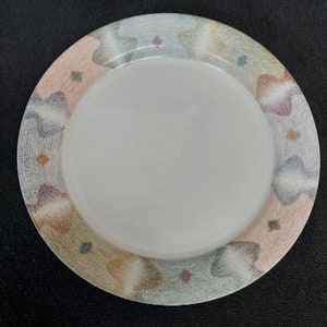 May include: A white ceramic dinner plate with a colorful abstract design in shades of pink, blue, green, and brown. The design features a swirling pattern of clouds and leaves.