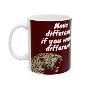 Peut inclure: Mug en céramique blanche avec une anse. Le mug présente un motif de léopard et le texte "Move different if you want different" en blanc. Le fond est de couleur rouge foncé.