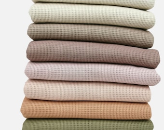 May include: A stack of ten different coloured waffle knit fabrics. The colours are beige, light brown, brown, pink, light pink, peach, orange, green, and grey.