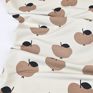 Op de afbeelding: Een crèmekleurige stof met een herhalend patroon van bruine appels. De appels hebben zwarte stelen en bladeren.