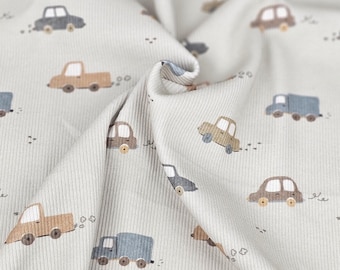 May include: A close-up of a light gray fabric with a repeating pattern of brown and blue cars and trucks. The fabric has a ribbed texture.