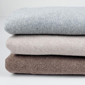 Könnte beinhalten: Drei gefaltete Decken in verschiedenen Brauntönen, Beige und Grau. Die Decken sind aus einem weichen, flauschigen Material.