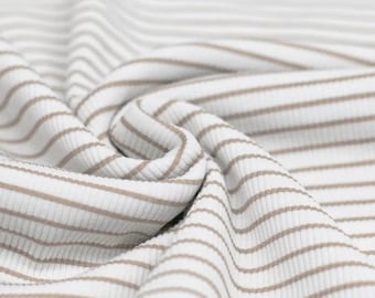 May include: White and beige striped fabric with a ribbed texture. The fabric is folded and draped, showing the pattern and texture.