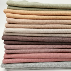 Könnte beinhalten: Ein Stapel Stoffmuster in verschiedenen Brauntönen, Rosa und Grün. Der Stoff ist weich und gestrickt.