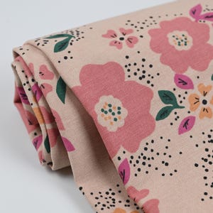 Könnte beinhalten: Gerollter Stoff mit floralem Muster. Das Design umfasst große rosa Blüten, kleinere rosa und orangefarbene Blüten, grüne Blätter und schwarze Sprenkel auf beigem Hintergrund. Der Stoff ist gefaltet und zeigt die Musterwiederholung.
