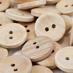Könnte beinhalten: Ein Haufen natürlicher Holzknöpfe mit zwei oder drei Löchern. Die Knöpfe sind rund und haben eine glatte, leicht strukturierte Oberfläche.