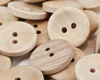 Può includere: Un mucchio di bottoni in legno naturale con due o tre fori. I bottoni sono rotondi e hanno una superficie liscia leggermente ruvida.