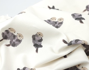May include: Off-white fabric with a repeating pattern of watercolor otters in shades of gray and brown. The otters are depicted in various poses, some holding hands. The fabric has a soft, textured appearance, suggesting a comfortable material.