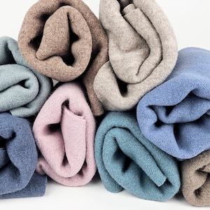 Könnte beinhalten: Eine Ansammlung von gerollten Stoffstücken in verschiedenen Farben, darunter Braun, Beige, Hellblau, Altrosa und Blaugrün. Jedes Stück weist eine weiche, gefilzte Textur mit sichtbaren Fasern auf, die in einem dichten, überlappenden Haufen angeordnet sind.