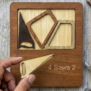 May include: Wooden puzzle featuring four saw-shaped pieces, one being held. The puzzle is in a wooden frame, with the text "4 Saws 2". A measuring tape, pencil, screws, and a caliper are also present.