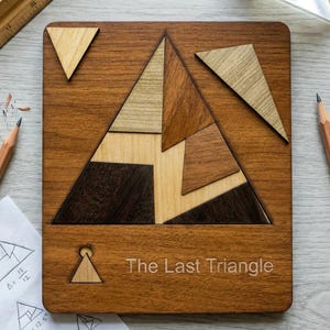 Op de afbeelding: Houten puzzel met een driehoekig ontwerp, met verschillende houttinten. De puzzel is getiteld "The Last Triangle" en bevat losse stukken. Een liniaal, potloden en een prisma zijn ook aanwezig.