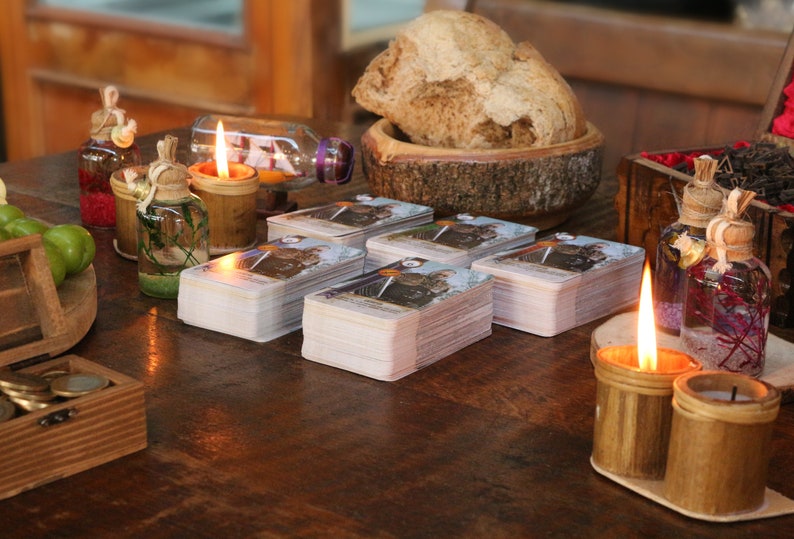 May include: A wooden table setting with lit candles, tarot cards, and decorative bottles. A wooden bowl holds a loaf of bread. The scene evokes a mystical or spiritual theme.