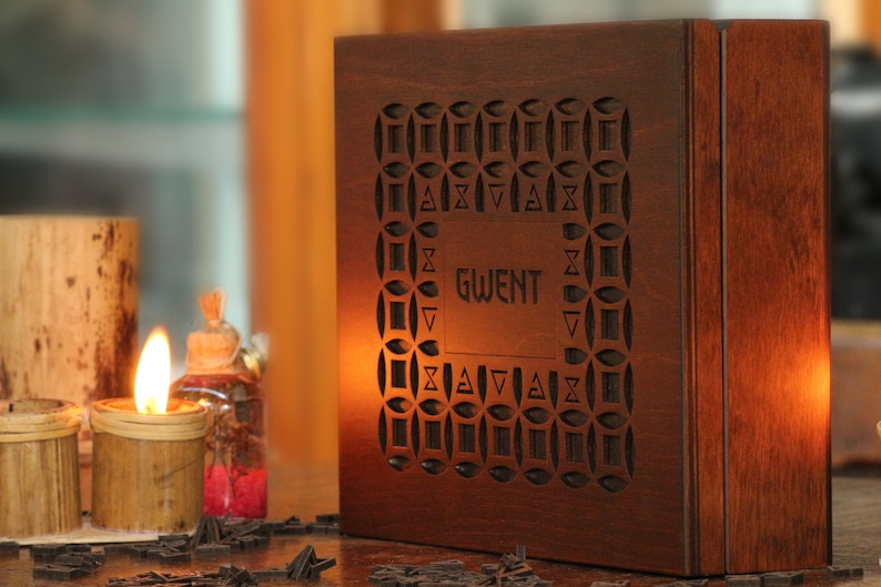 May include: A wooden box with the word "GWENT" carved into the front. The box has a decorative geometric pattern around the text. A lit candle and other decorative items are in the background.