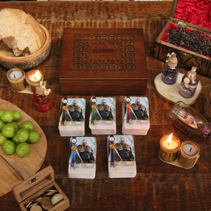 May include: A wooden table setting with a variety of items. Includes a wooden box, playing cards, fruit, bread, candles, and decorative bottles. The scene evokes a medieval or fantasy theme, suitable for a board game or themed event.