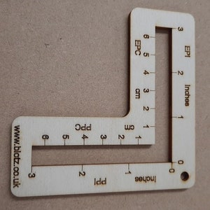 May include: A wooden ruler with markings in inches and centimetres. The ruler has two scales, one for measuring the width of fabric in "EPI" and the other for measuring the length of fabric in "EPC". The ruler also has a website address printed on it: www.blotz.co.uk.