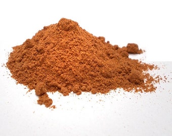 May include: A pile of ground cinnamon spice, a reddish-brown color, on a white surface.