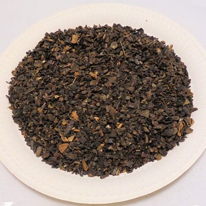 May include: A close-up of a pile of loose leaf black tea with small pieces of dried fruit and herbs.