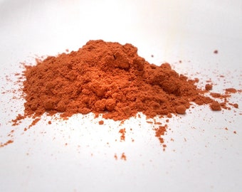May include: A pile of bright orange powder on a white surface.