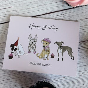 May include: A pink birthday card with a happy birthday message and four dogs wearing hats and holding cupcakes. The card says "From the Squad" at the bottom.