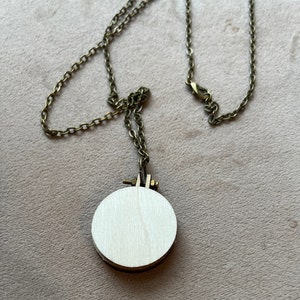 Pu&ograve; includere: Una collana con catena dorata e un ciondolo rotondo in legno. Il ciondolo &egrave; vuoto e pronto per essere ricamato.