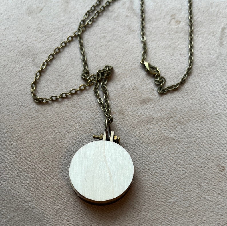 Pu&ograve; includere: Una collana con catena dorata e un ciondolo rotondo in legno. Il ciondolo &egrave; vuoto e pronto per essere ricamato.