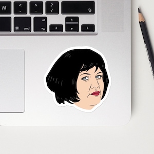 Puede incluir: Una pegatina con una ilustración de dibujos animados de una mujer con el pelo negro corto y una expresión seria. Lleva una camisa blanca y tiene los labios rojos.