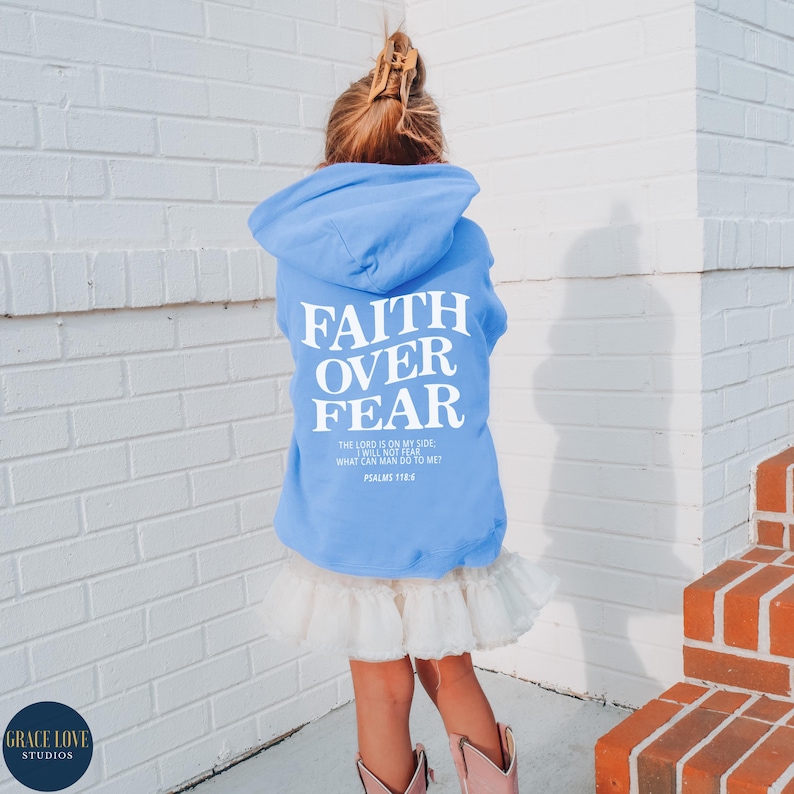 Puede incluir: Una sudadera con capucha azul claro con el texto "FAITH OVER FEAR" en blanco. La sudadera tambi&eacute;n incluye el texto "THE LORD IS ON MY SIDE, I WILL NOT FEAR, WHAT CAN MAN DO TO ME? PSALMS 118:6" en blanco m&aacute;s peque&ntilde;o.