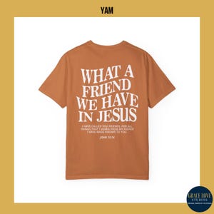 Peut inclure: Un t-shirt &agrave; manches courtes de couleur rouille avec un imprim&eacute; blanc qui dit "Quel ami nous avons en J&eacute;sus". L'impression comprend &eacute;galement un verset biblique, "Jean 15:14".