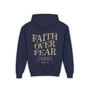 Puede incluir: Sudadera con capucha azul marino con una impresi&oacute;n en color tostado que dice "FAITH OVER FEAR" y la escritura "El Se&ntilde;or es mi ayuda, no temer&eacute;. &iquest;Qu&eacute; me puede hacer el hombre? Salmos 118:6"