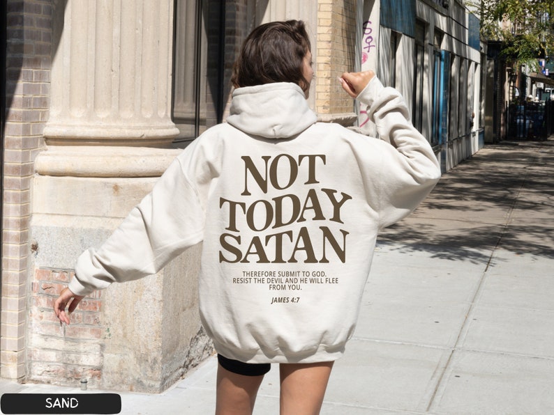 May include: A beige hoodie with the text "NOT TODAY SATAN" in brown lettering. The text "THEREFORE SUBMIT TO GOD. RESIST THE DEVIL AND HE WILL FLEE FROM YOU. JAMES 4:7" is printed in smaller brown lettering below the main text.