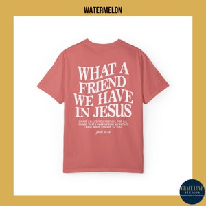 Peut inclure: Un t-shirt rose corail avec un imprim&eacute; graphique blanc qui dit "Quel ami nous avons en J&eacute;sus". Le graphique comprend &eacute;galement le verset biblique Jean 15:14.