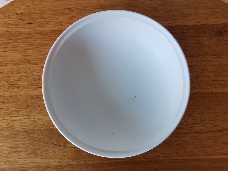 May include: A white, round ceramic plate with a slightly raised rim. The plate is centered on a wooden surface. The plate's interior is smooth and empty, ready for food. The plate is approximately 10 inches in diameter.