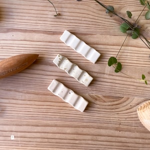 May include: Three white ceramic chopstick rests with a wavy design. The rests have a speckled pattern with brown and white flecks. The rests are on a light brown wooden surface.