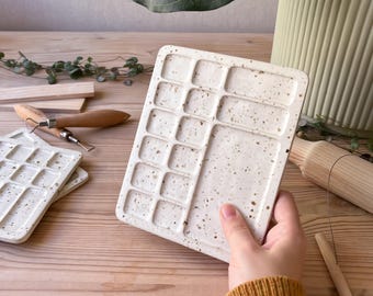 May include: White ceramic paint palette with 16 wells. The palette has a speckled finish and is perfect for holding watercolors or acrylic paints.