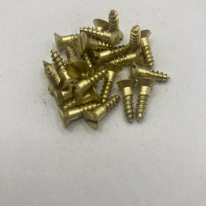 May include: A pile of brass screws with a flat head and a slotted drive. The screws are approximately 1 inch long.