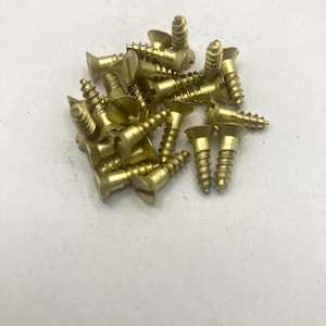 May include: A collection of small, gold-colored metal screws with flat, countersunk heads and single-slot drives. The screws feature threaded shanks and are arranged in a loose pile, showing their metallic finish and pointed tips.