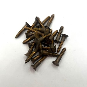 May include: A pile of antique brass wood screws with slotted heads. The screws have a dark, aged appearance, with visible threads and flat, slightly tapered heads. The screws are scattered against a white background.