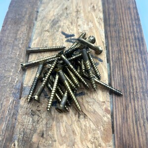 May include: A collection of brass-colored metal screws with flat heads and threaded shanks, arranged in a loose pile. Each screw features a pointed tip and a spiral design along the shaft, showing a metallic finish with visible signs of wear.