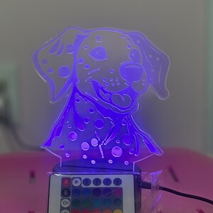 May include: A white dalmatian dog night light with a purple glow. The light has a remote control with multiple colour options, including white, red, green, blue, and purple.