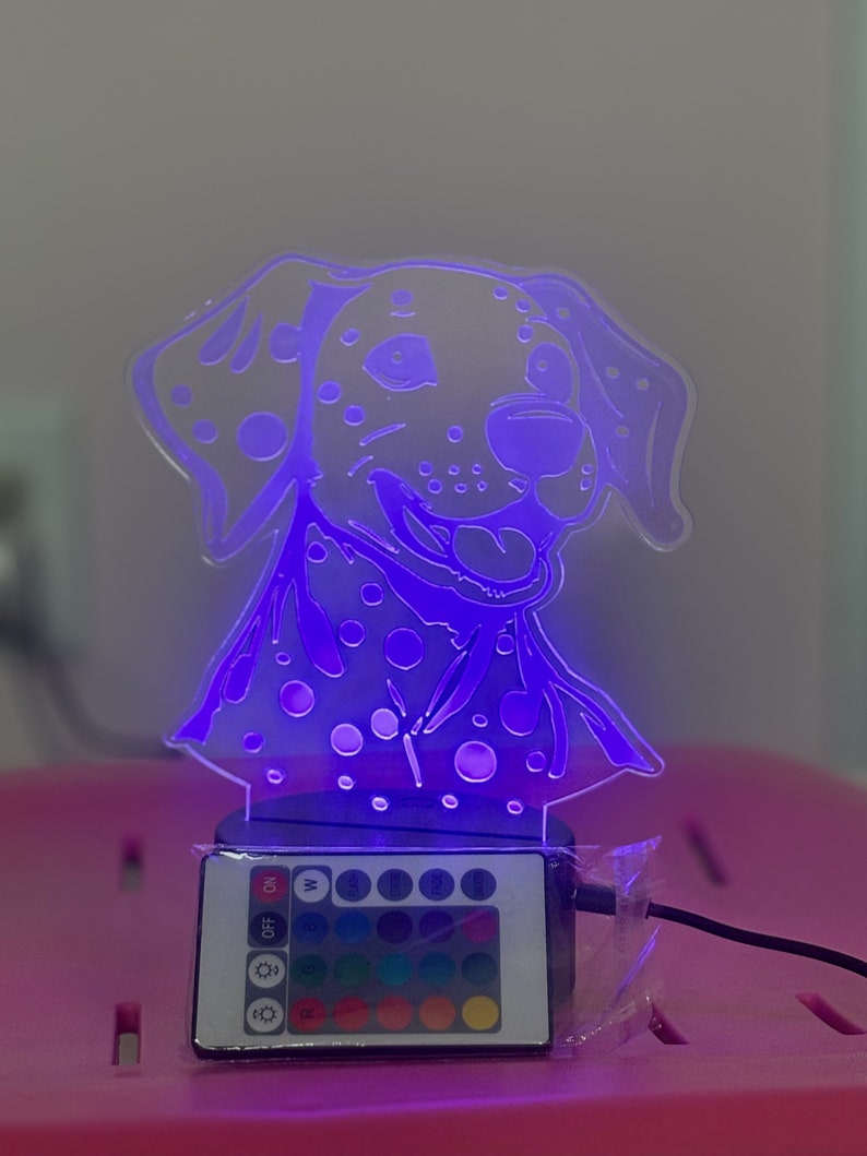 May include: A white dalmatian dog night light with a purple glow. The light has a remote control with multiple colour options, including white, red, green, blue, and purple.