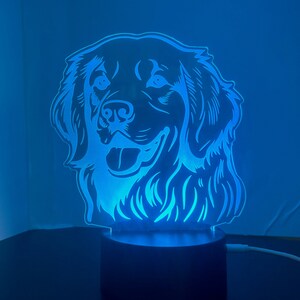 May include: A blue LED night light shaped like a dog's head. The dog has a happy expression and is facing forward. The light is on a black base.