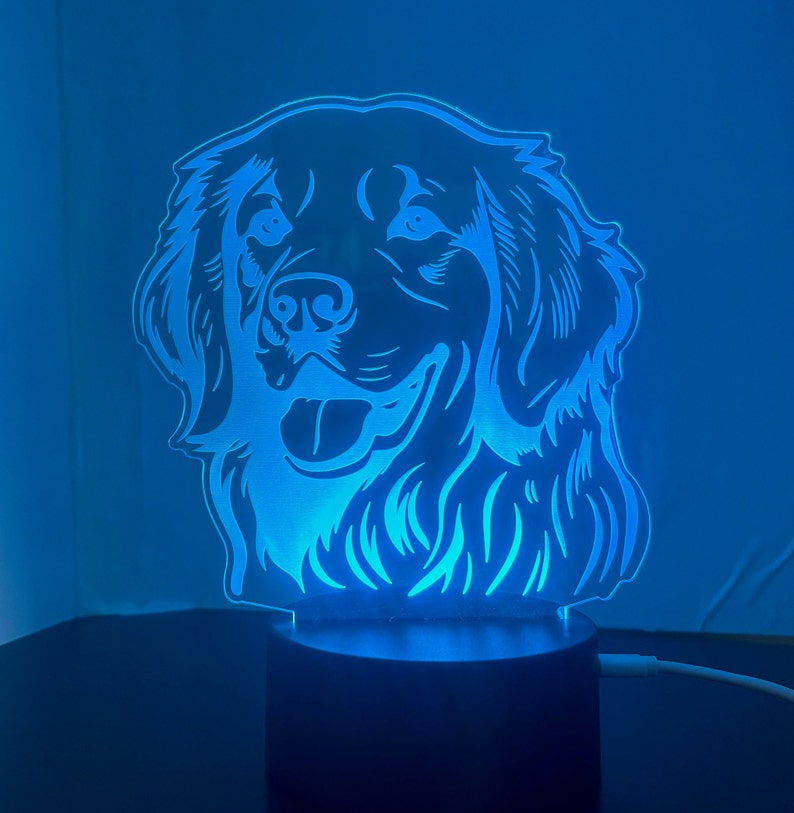 May include: A blue LED night light shaped like a dog's head. The dog has a happy expression and is facing forward. The light is on a black base.