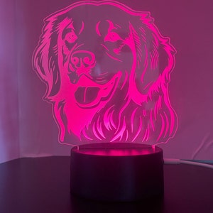 May include: A pink acrylic night light shaped like a golden retriever dog's head. The light is on a black base.