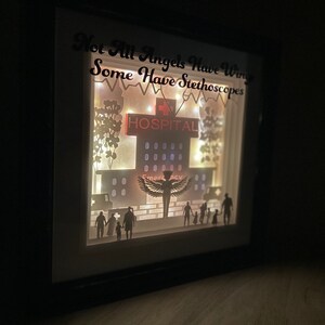 May include: A white light-up shadow box with a silhouette of a hospital building, a nurse with wings, and a family. The text "Not All Angels Have Wings Some Have Stethoscopes" is written at the top of the box.