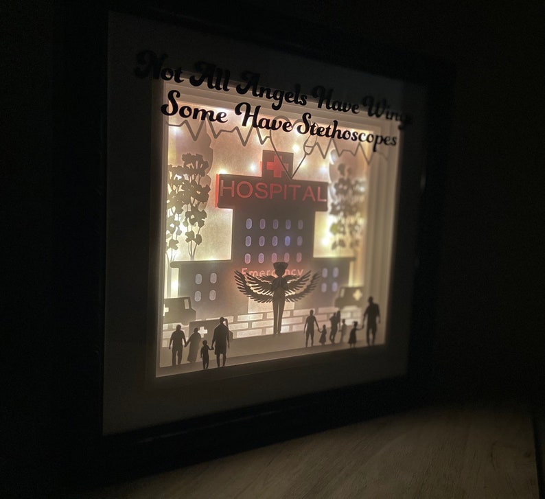 May include: A white light-up shadow box with a silhouette of a hospital building, a nurse with wings, and a family. The text "Not All Angels Have Wings Some Have Stethoscopes" is written at the top of the box.